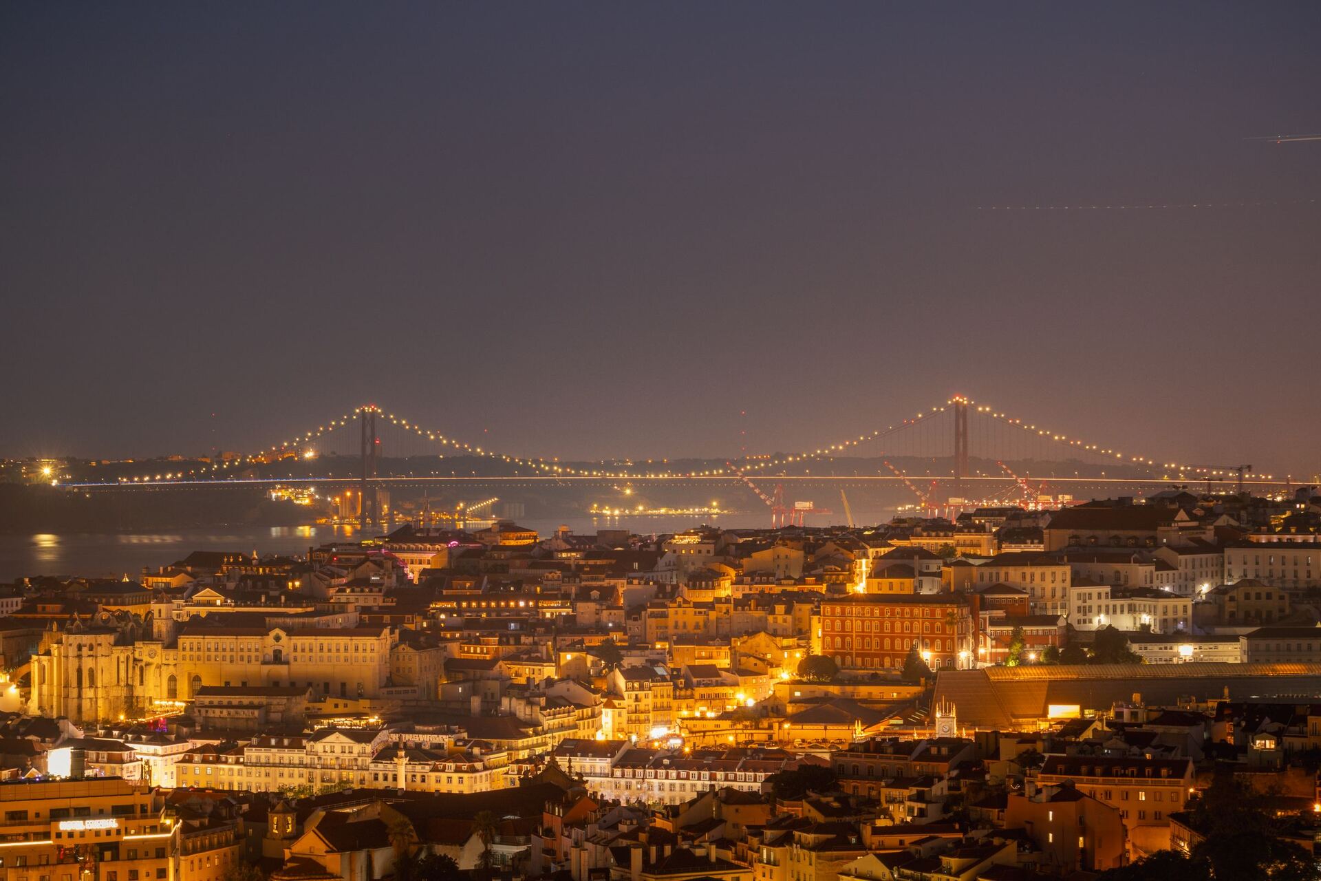 Lisbon and the illuminated 25 de Abril Bridge at night.